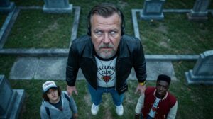 Mann im Hellfire-Club-Shirt und zwei Jugendliche auf einem Friedhof aus der Vogelperspektive